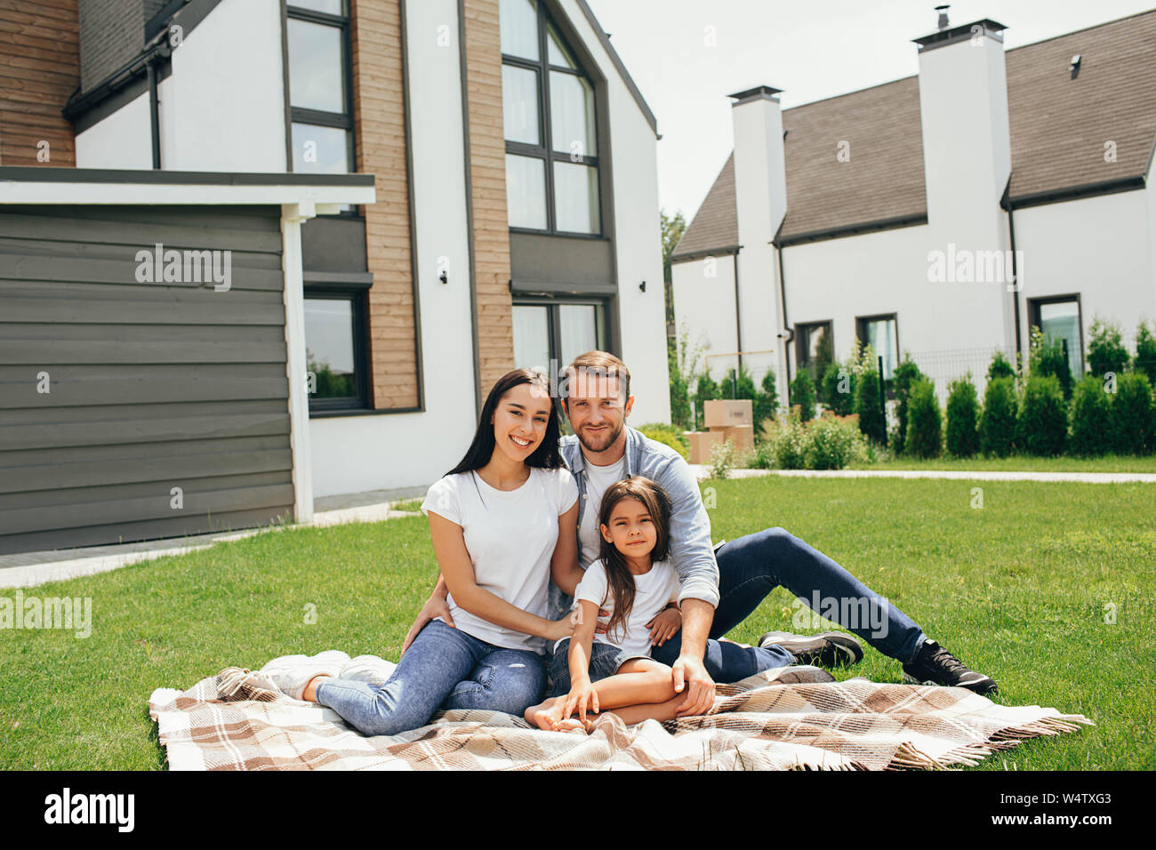 Familie sitzt auf Rasen im Hinterhof, großes, modernes Haus auf Hintergrund Stockfoto