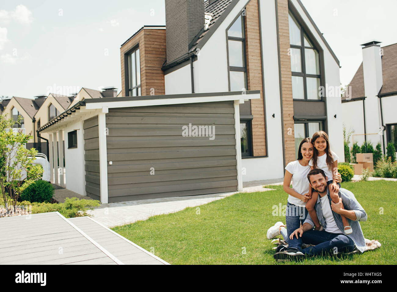 Familie sitzt auf Rasen im Hinterhof, großes, modernes Haus auf Hintergrund Stockfoto