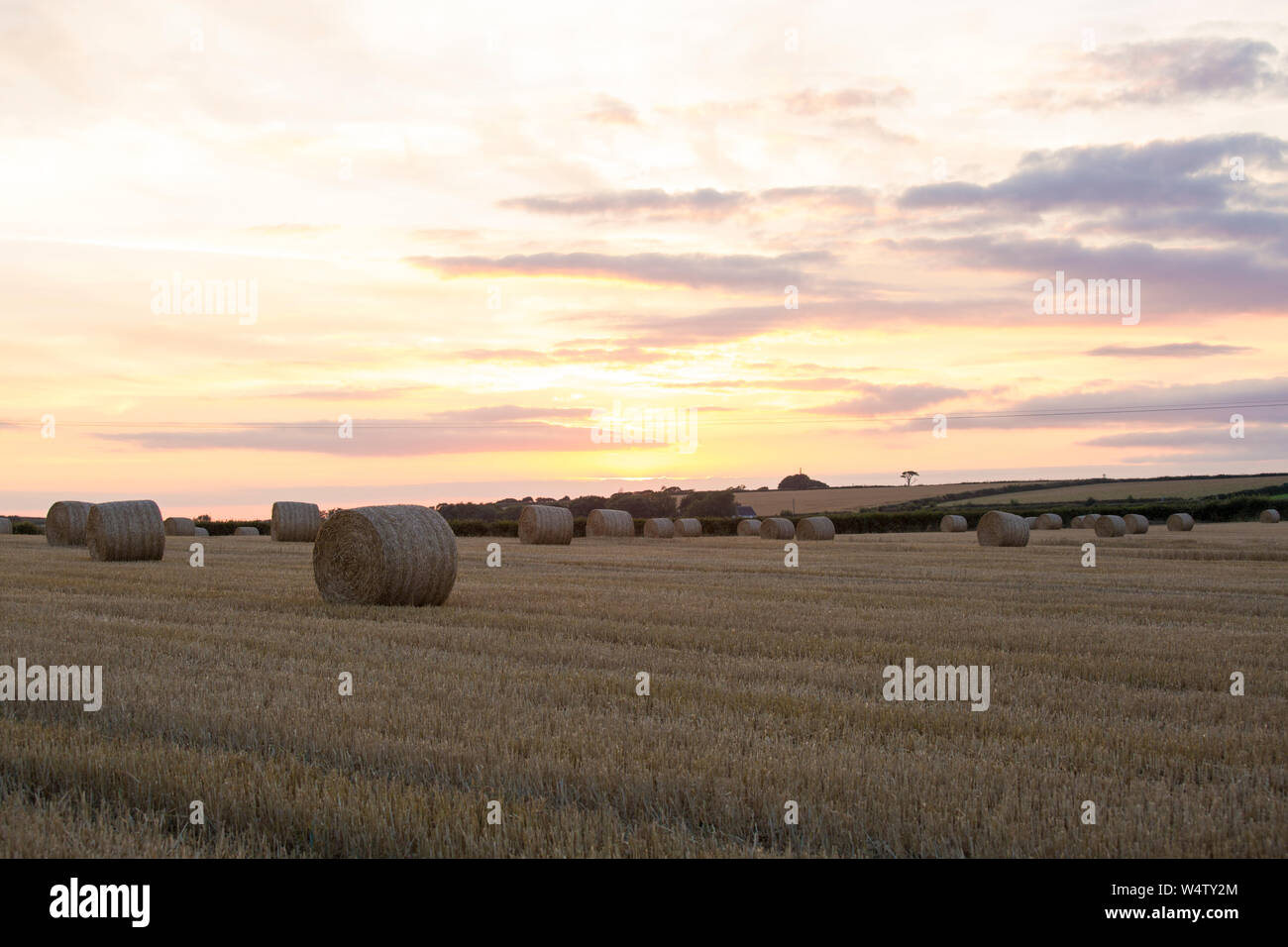 Sonnenuntergang über einem Gebiet der Vor kurzem Schnitt Stroh mit runden Strohballen in die Stoppeln Feld Stockfoto