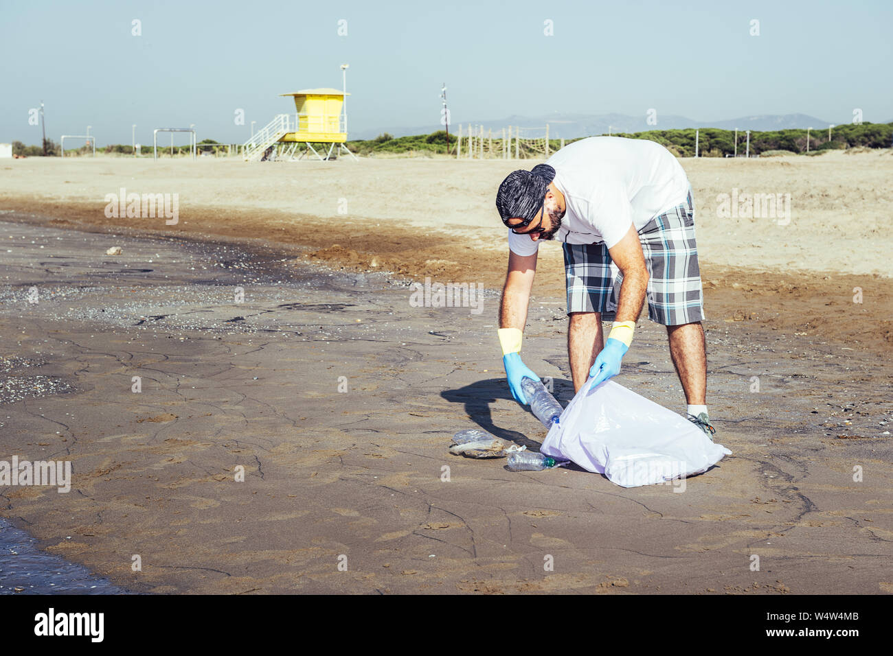 Mann sammeln von Kunststoffen, die den Ozean in Plastikbeutel verschmutzen, Menschen zu helfen, um die Natur sauber und Abholung der Abfälle aus Strand, Volunteer Camp Stockfoto