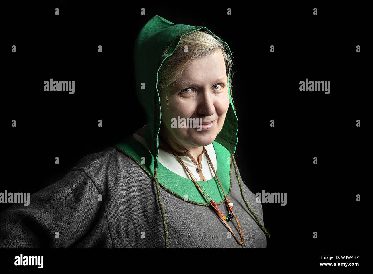 Reife blonde Frau in einem historischen Kostüm der Wikingerzeit lächelnd. close-up Portrait auf schwarzem Hintergrund Stockfoto