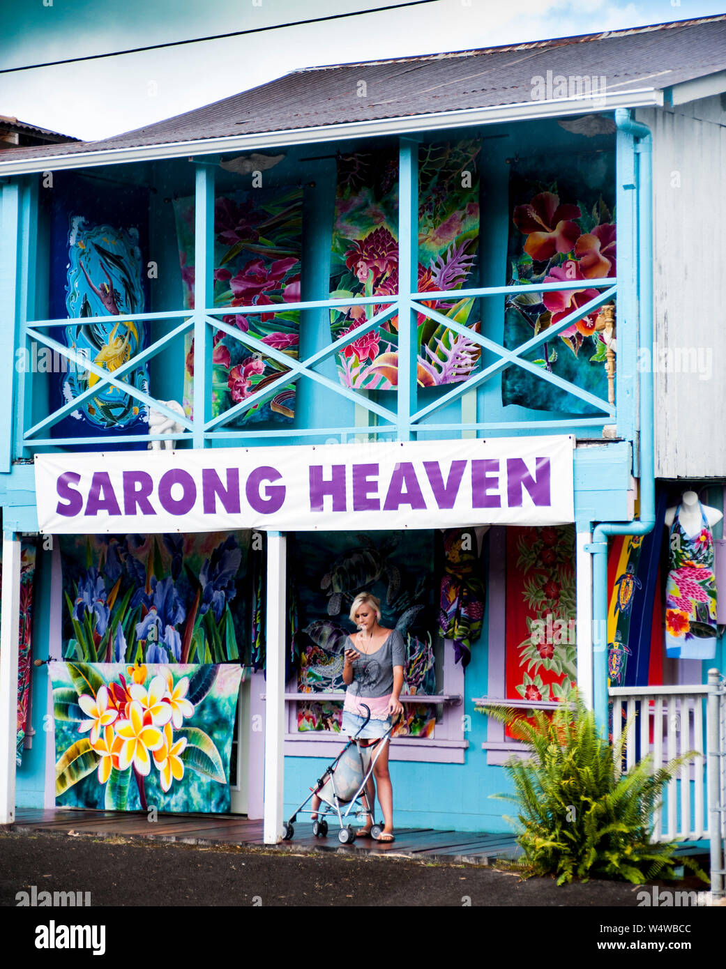 Junge Frau mit einem Kinderwagen überprüft Ihr Handy beim Einkaufen in der Stadt an der Hilo auf der grossen Insel von Hawaii Stockfoto