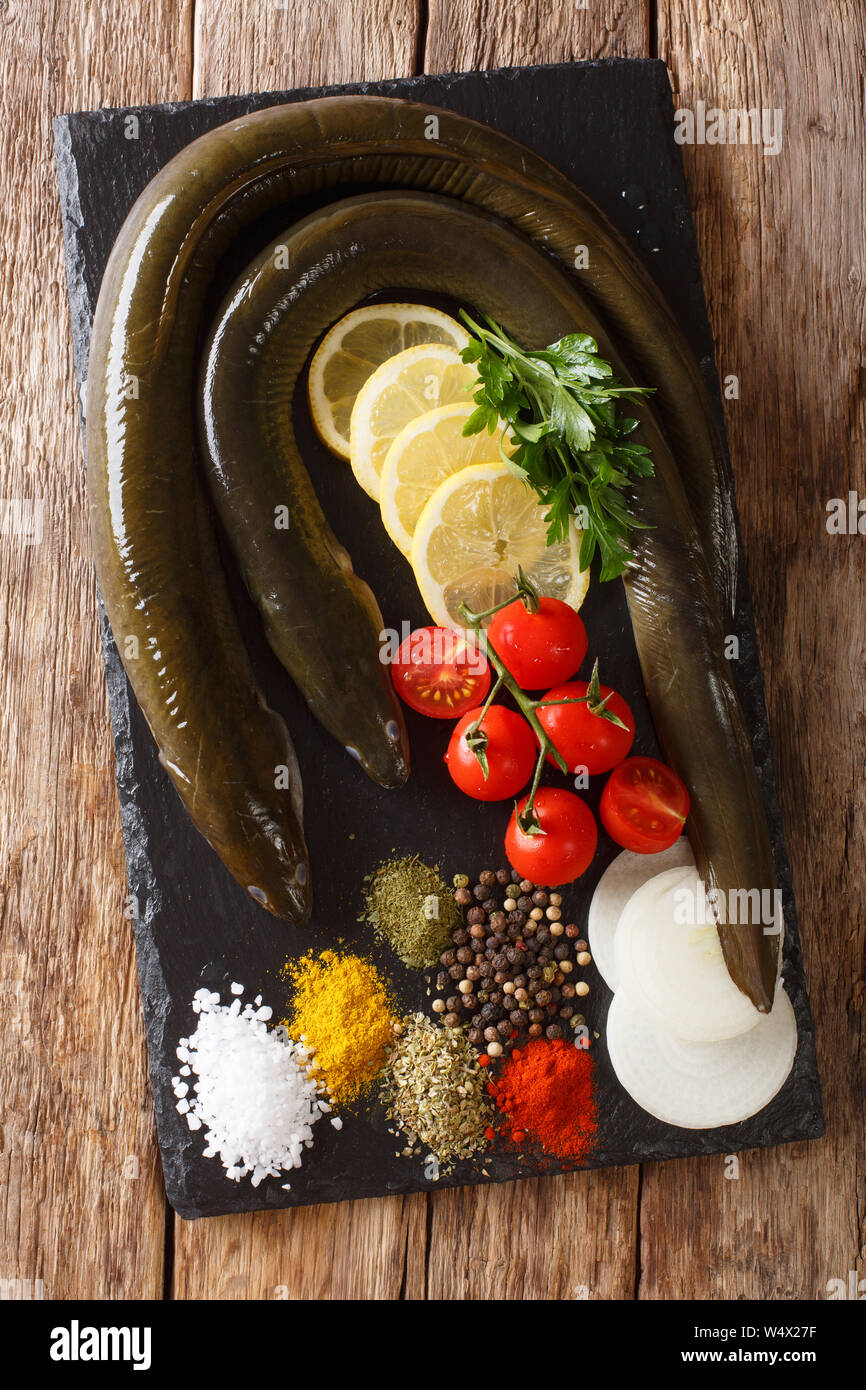 Raw Aal mit Gewürzen, Gemüse und Zitrone close-up auf einer Schiefertafel Board auf dem Tisch. Vertikal oben Ansicht von oben Stockfoto