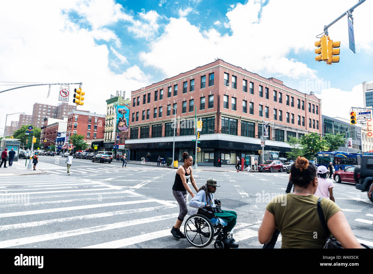 New York City, USA - August 1, 2018: Junge Frau treibt ein Rollstuhl mit einem alten schwarzen Mann auf einer Straße in Harlem, New York City, USA Stockfoto