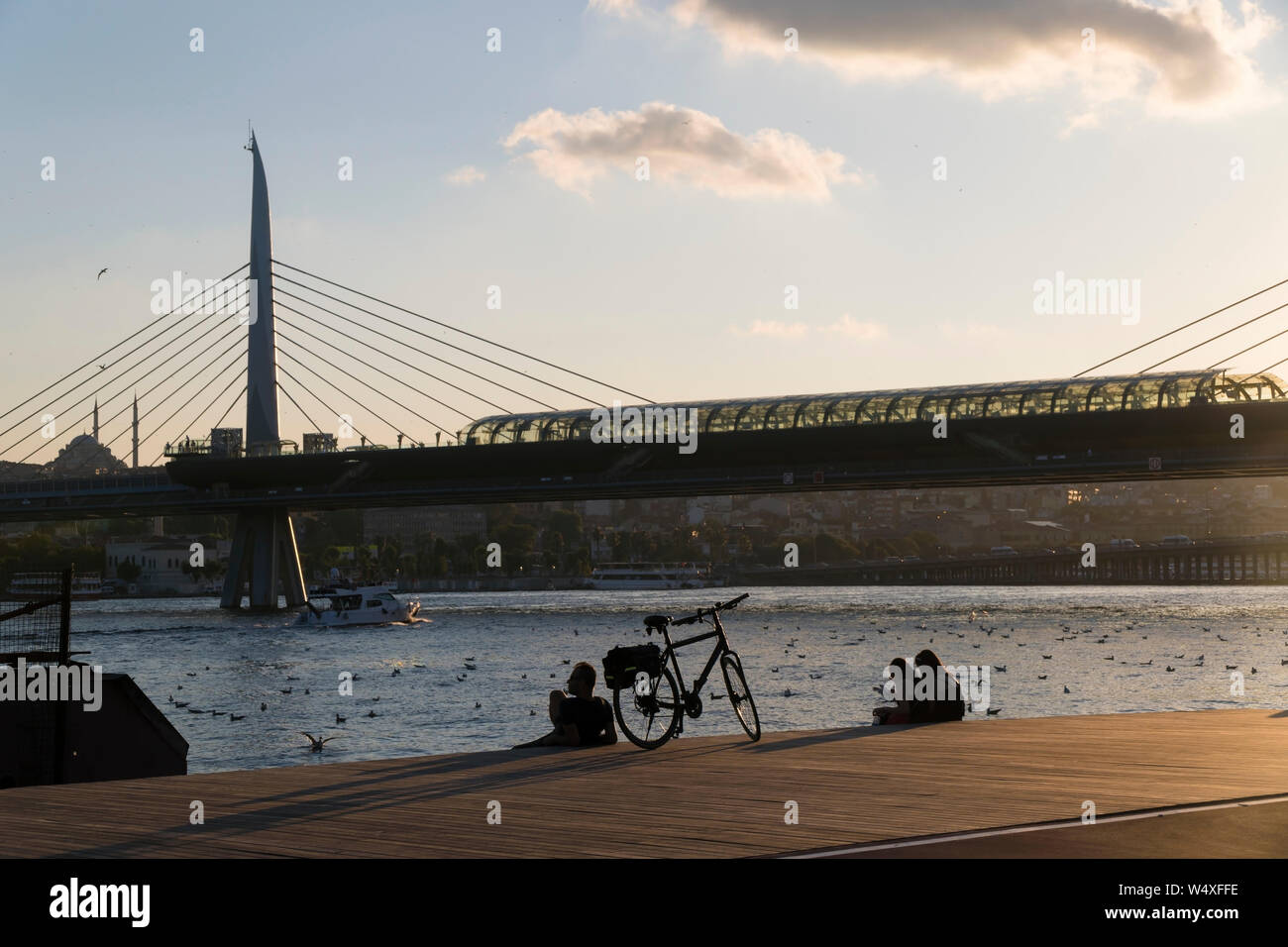 Istanbul, Türkei - 19 Juli, 2019: ein Biker, sein Fahrrad und zwei junge Frauen sind an der Küste des Goldenen Horns auf Holzboden in Sonnenuntergang. Stockfoto