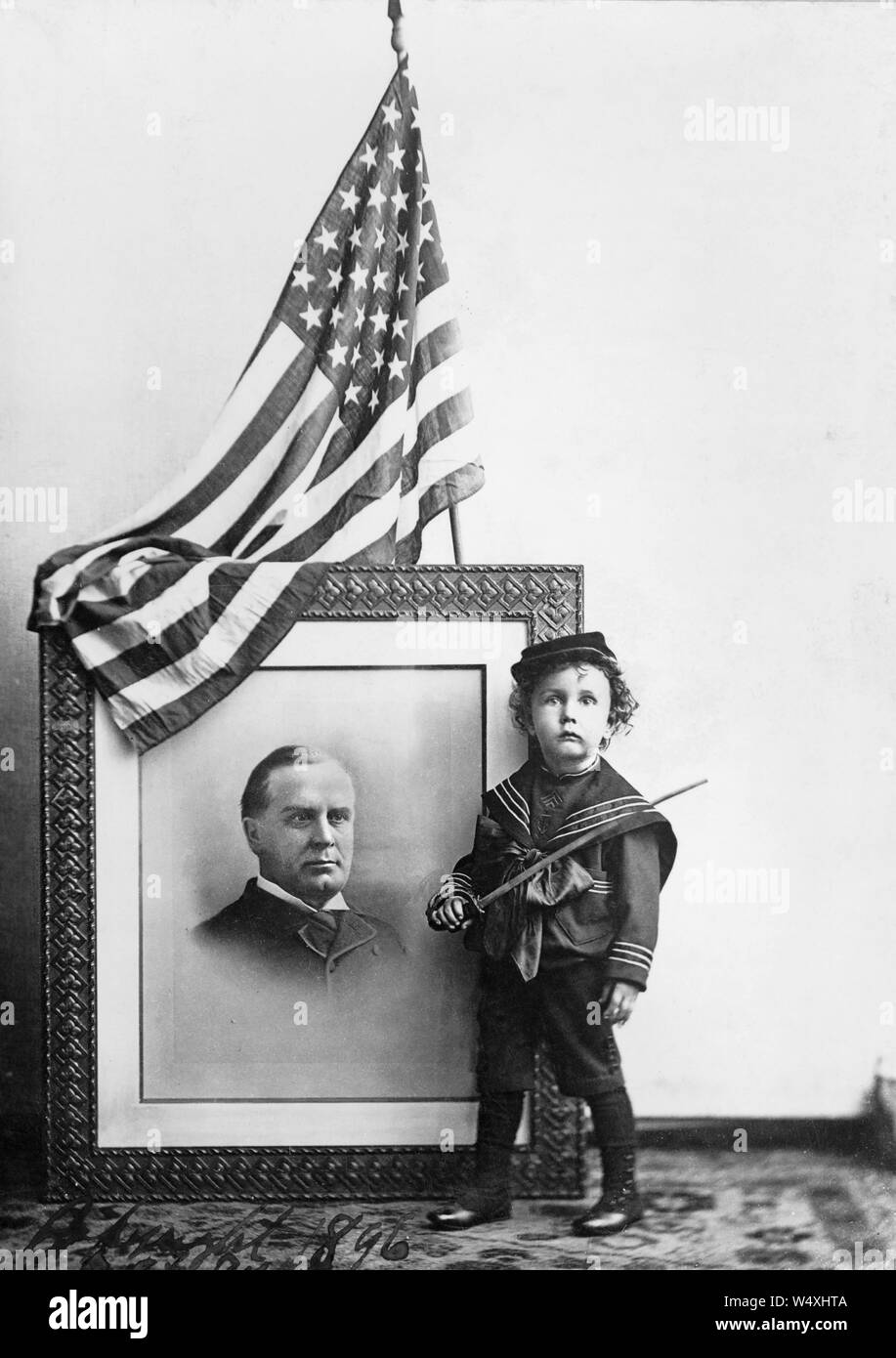 Junge in Sailor Uniform holding Schwert vor der Fahne - drapiert, mit Kopf und Schultern im Porträt von William McKinley, 1896 Stockfoto