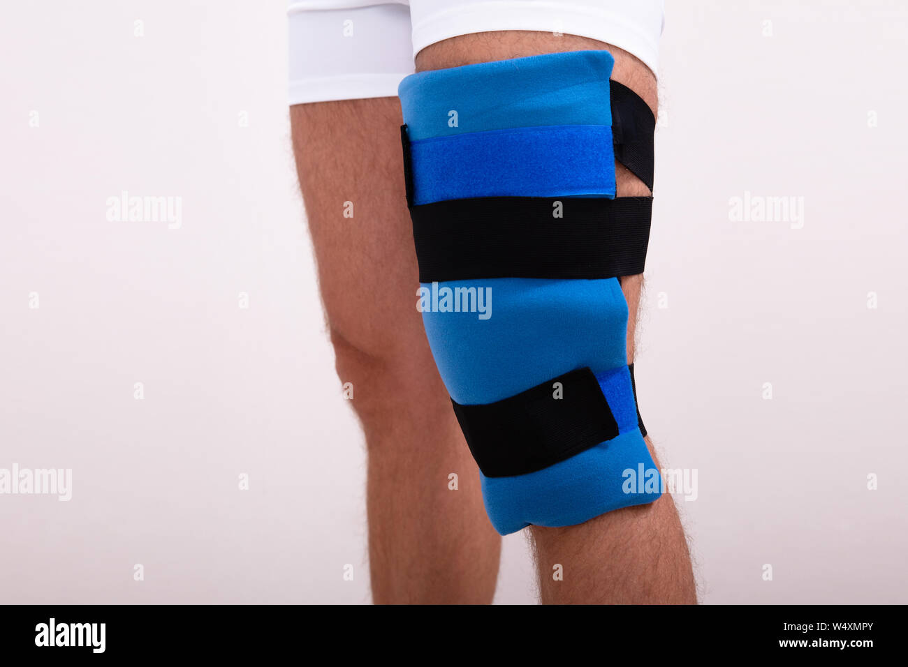 Close-up von einem Mann mit blauen Knie Ice Pack gegen den weißen Hintergrund Stockfoto