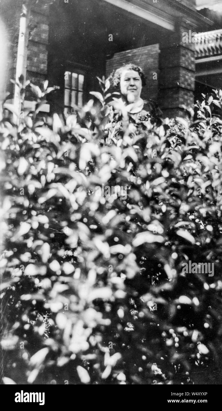 Reife Frau vor einem Haus in Detroit, Michigan und Suchen über eine Hecke, Winkel, Ansicht, 1927. () Stockfoto