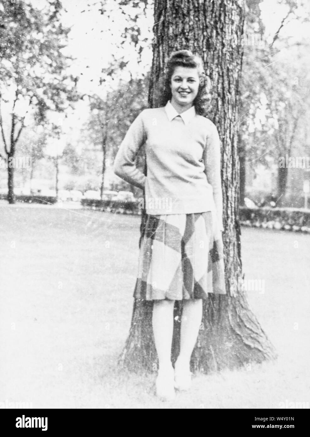 Junge Frau mit Bluse und Rock, vor einem Baum im Freien posieren, lächelnd mit der einen Hand hinter den Rücken und die andere an Ihrer Seite, 1950. () Stockfoto