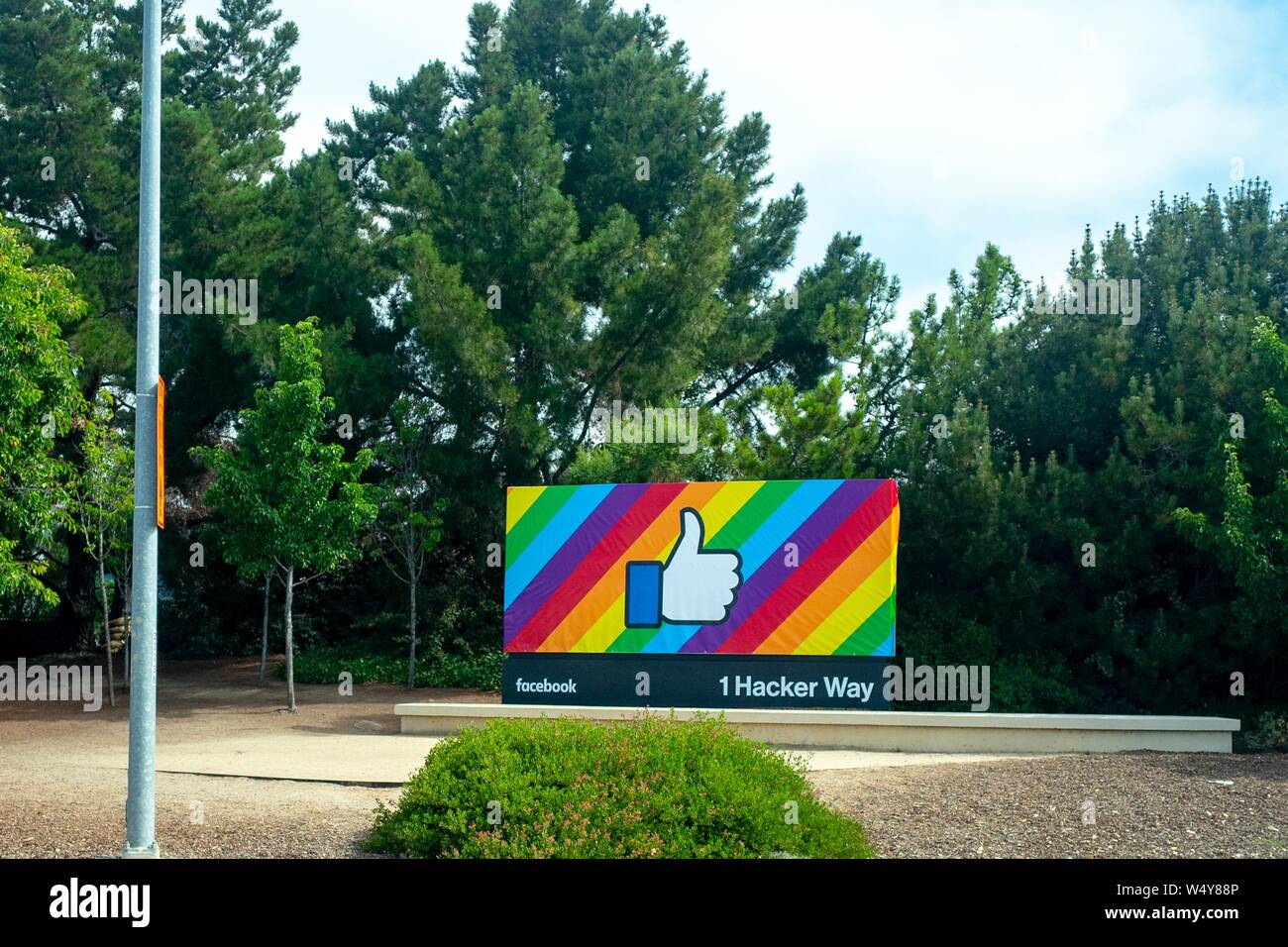 Schild mit Logo am Eingang zum Hauptquartier von Facebook Inc. unter 1 Hacker in Menlo Park, Kalifornien, mit einem Regenbogen Flagge design in der Feier des Stolzes Monat, 19. Juni 2019 eingerichtet. () Stockfoto