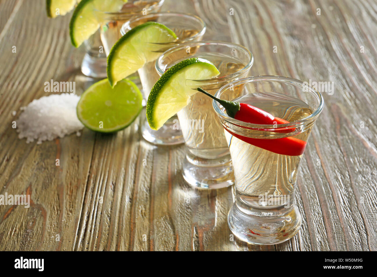 Schüsse von leckeren Tequila mit Kalk, Salz und Chili auf hölzernen Tisch Stockfoto