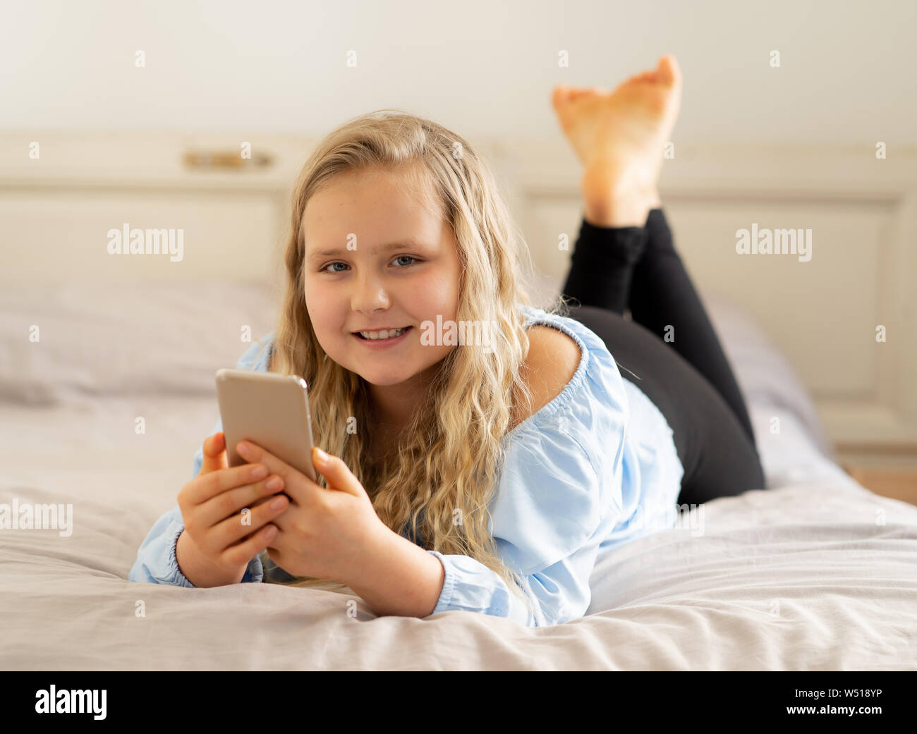 Schöne blonde glücklichen kleinen Mädchen spielen auf dem Handy. Niedlichen Kind im Internet mit Smartphone social media App im Bett zu Hause liegen zu plaudern. Stockfoto
