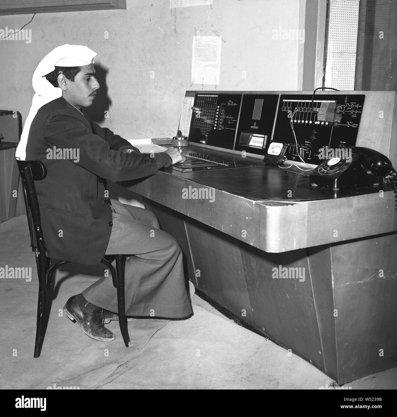 1960, historische, eine männliche Ausstrahlung Techniker, iin traditionelle arabische Kleidung von thoe und kufiya Kopfschmuck, mit Blazer, Arbeiten an den Kontrollen einer Broadcast Konsole im TV-Studio, Saudi-Arabien. Stockfoto