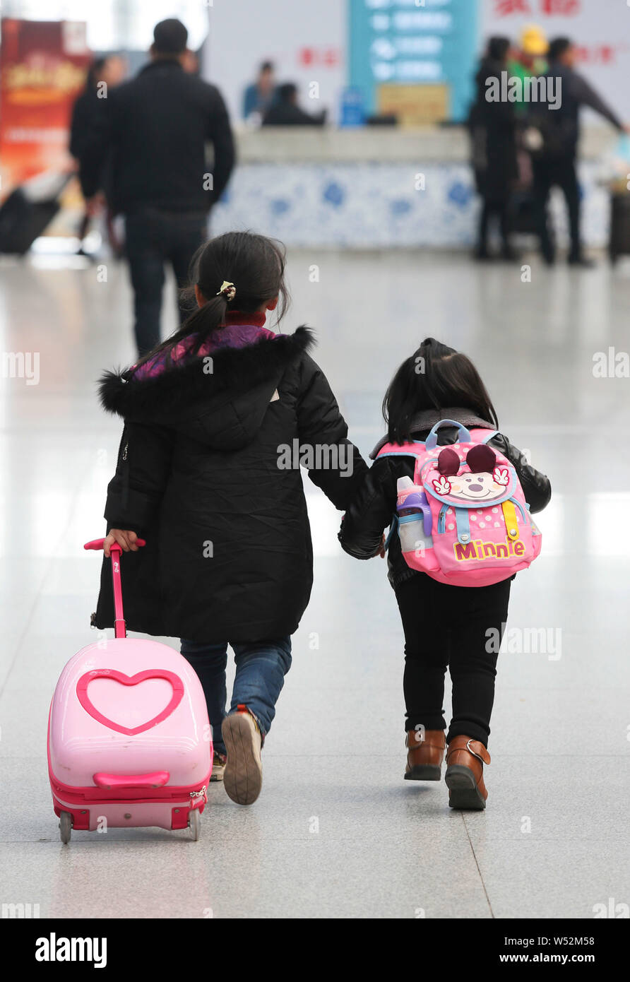 Ein kleines chinesisches Mädchen geht mit ihrer jüngeren Schwester, wie sie und ihre Eltern auf dem Weg nach Hause mit dem Zug für das chinesische Mondjahr werden während der Stockfoto