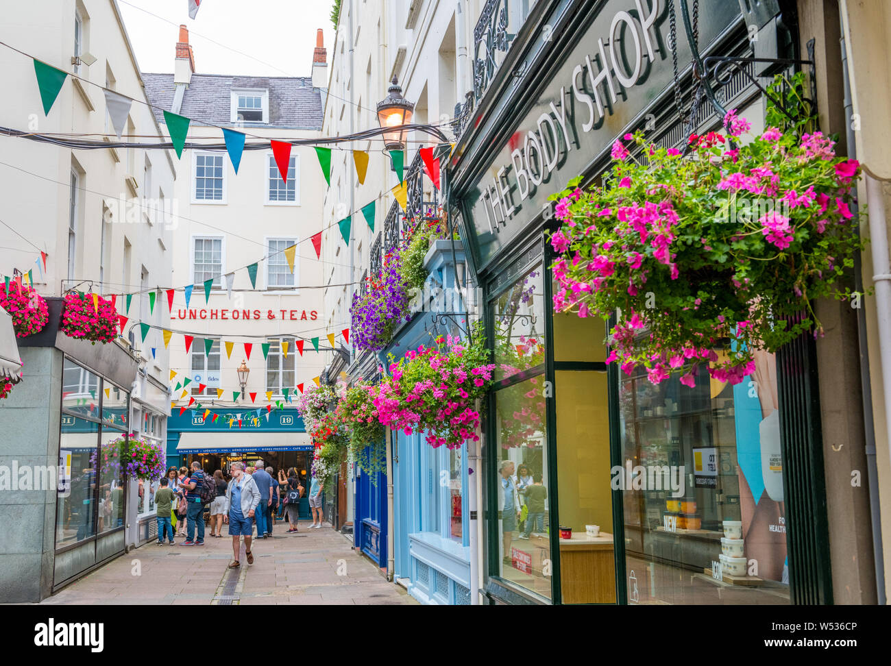Hängenden Blumenkörben außerhalb der Geschäfte entlang der schmalen Einkaufsstraßen von St Peters Port, Guernsey. Stockfoto