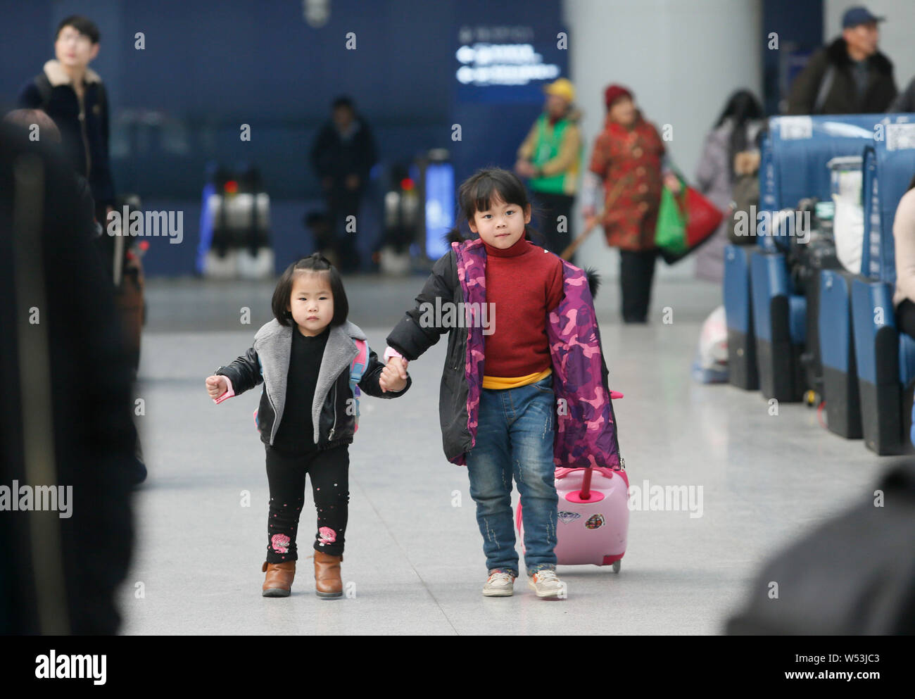 Ein kleines chinesisches Mädchen geht mit ihrer jüngeren Schwester, wie sie und ihre Eltern auf dem Weg nach Hause mit dem Zug für das chinesische Mondjahr werden während der Stockfoto