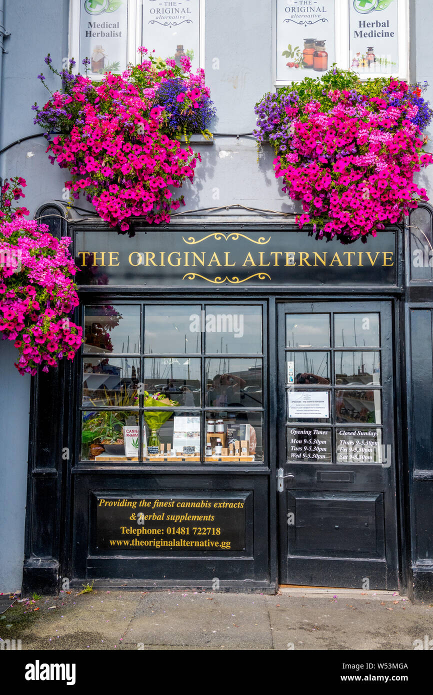 Hängende Körbe von Blumen über eine Apotheke Shop" der ursprünglichen Alternative', die Cannabis Extrakte und pflanzliche Präparate auf Guernsey. Stockfoto