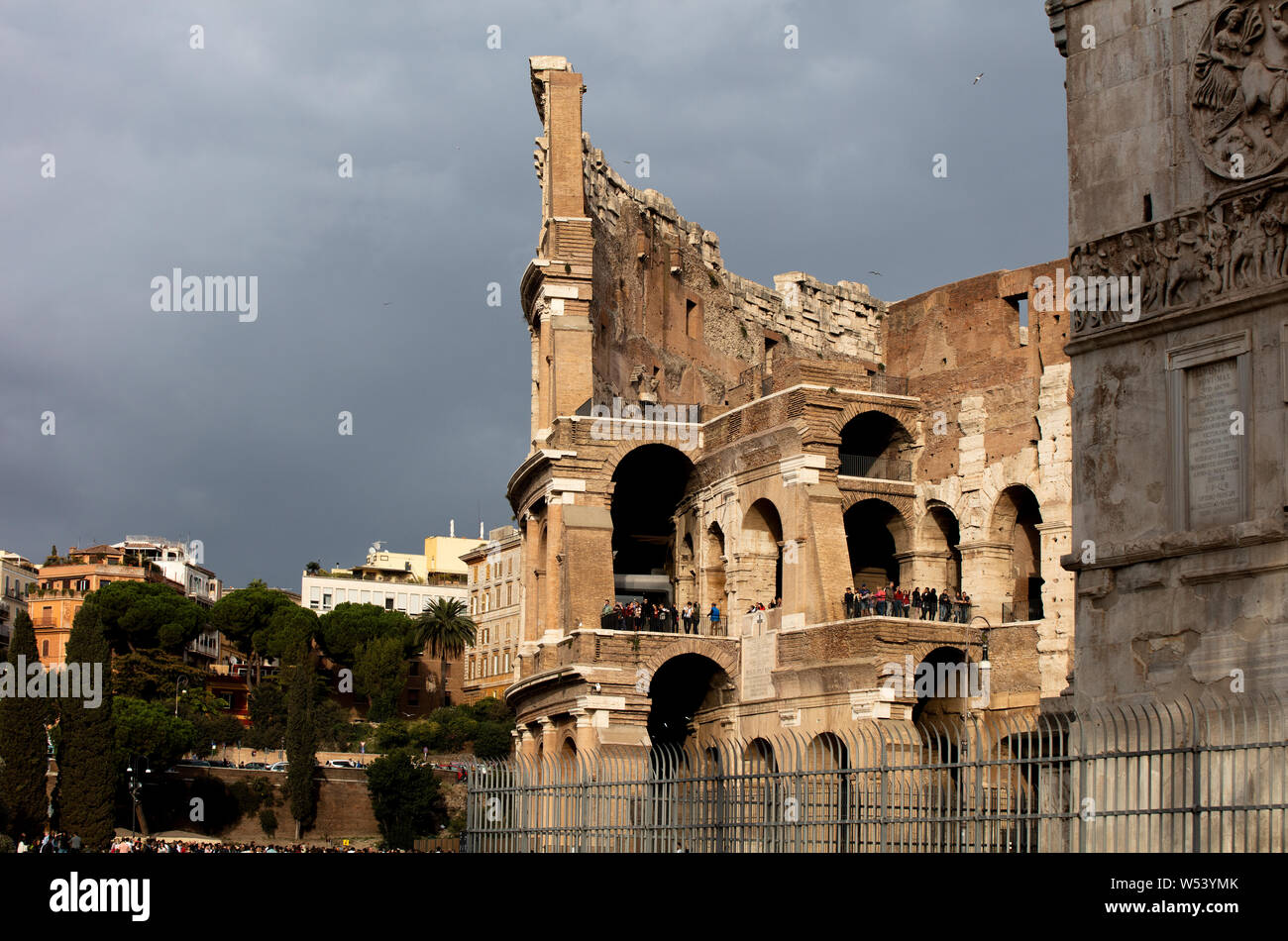 Das Äußere des Kolosseum im Abendlicht mit Touristen Anzeigen der Ruinen. Den Himmel hinter dunkel, grau und stürmisch. Stockfoto