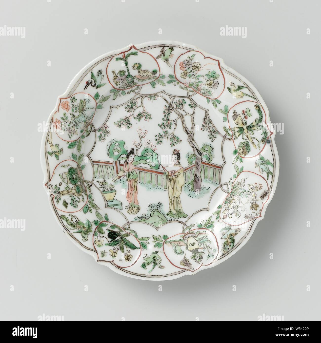 Mit zwei Damen in einem eingezäunten Garten, Antiquitäten und Blume sprays Platte, Porzellan Teller mit gezacktem Rand, in unterglasur Blau und auf der Glasur Blau, Rot, Grün, Gelb, Weiß und Schwarz lackiert. Auf dem Regal ein formschönes Medaillon mit zwei Damen (lange Zeilen), eines mit einem Ventilator und einer mit einer Kanne, in einem umzäunten Garten mit einem Blumentopf, Felsen und Bäumen, an der Wand und Rand pfirsich-förmige Kartuschen gefüllt mit einer Blume Zweig mit Insekten- oder Antiquitäten (Vase, Pfauenfedern, Bücher, ruyi-Zepter, Stativ, Statue eines Löwen und Dreibeinige Kröte), unter die Boxen von fliegenden Vögeln, die zurück Stockfoto