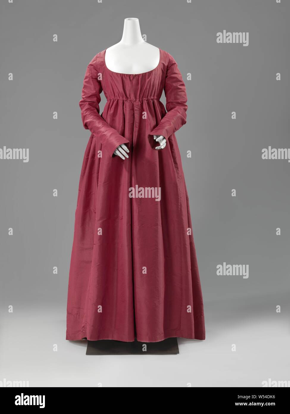 Kleid Kleid, Rot gerippt Seidenkleid mit hoher Taille, langen, schmalen Ärmel, Rautenförmigen wieder einsetzen und kleinen Zug. Modell: Runder Ausschnitt mit Kordelverschluss, mitte vorne, oben aufgeteilt. Hohe Taille schließt mit Tunnel durch Baumwolle Ribbon. Ärmel Schnitt schräg auf das Gewinde mit Ellenbogen und Manschette, die über die Rückseite der Hand fallen. Rock besteht aus einem Gewebe (72 cm) in der Mitte der Vorder- und Rückseite, mit zwei Streifen von ca. 50 cm auf jeder Seite. In der Seitennaht eine lange offene aufgeteilt. Einen tiefen Kellerfalte in der Mitte mit drei flachen Falten oben auf jeder Seite. Zwei flache Falten an der Seitennaht. Inneren Körper Stockfoto