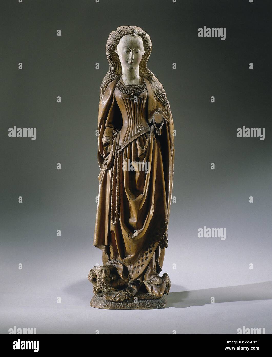 Katharina von Alexandria, sie steht mit beiden Beinen auf Kaiser Maxentius (?), Hat drehte ihren Kopf leicht nach rechts und schaut, vage lächelnd, etwas nach unten. Sie hält den linken Unterarm, gegenüber auf der rechten Seite. Die Haare an den Schläfen steigt und fällt in Wellen über den Rücken und die Schultern. Auf dem Kopf ein verwundeter Band mit Perlen und einige Rosetten. Das kleid Plissee auf der Vorderseite unter dem linken Arm gehalten wird, fällt über den liegenden Frost, lässt aber die Punkte ihrer Schuhe und ein Teil der Unterwäsche. Die Robe zeigt sowohl am Saum und an den Ärmeln für dekorative Steine. Ein Netzkabel Stockfoto