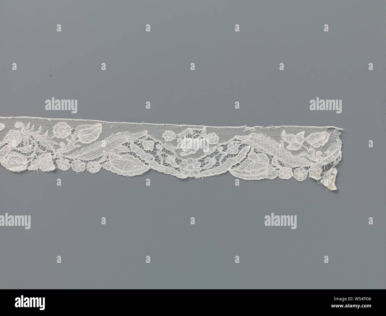 Streifen von klöppelspitze mit einem gewellten Band von Lancet Blätter und alle Arten von verschiedenen Blumen, Streifen von natürlichen Farben Brüssel Klöppelspitze. Das Muster besteht aus einem gewellten Band von länglichen Blättern und alle Arten von verschiedenen Blumen. In den Tälern gibt es immer einen oder ein paar Blumen mit großen Blättern, darunter zwei Rosette Blumen zwischen einem Gelappt herzförmigen Blätter, Rosette Blume mit einem Birnenförmigen Blatt und eine Blume mit sechs Spitzen Blütenblätter. Die Motive sind weitgehend der Bettwäsche mit offenen Kanten gearbeitet, einige Ausschnitte und mit geprägten Konturen verziert. Hier und da einem nettoeffekt befüllen Stockfoto