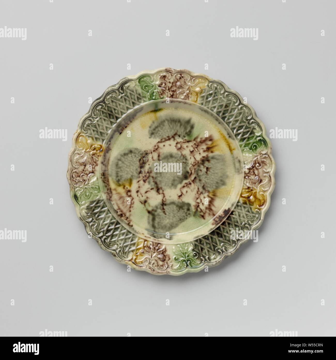 Platte von bunten Hard- abgefeuert, Steingut, Staffordshire, Platte von bunten Hard- feuerte Steingut. Die Grenze ist mit Verzierung, mit zwei symmetrischen floralen Mustern durchsetzt geprägte nebeneinander platziert. Die gekerbte Kante ist auf der Innenseite mit Voluten und Blattmotiven dekoriert. Die Platte ist mit eine gefleckte führen in Mangan Glasur, Grün, Grau und Gelb. Der Rücken ist in Mangan punktiert und hat einen Fuß Flanke, anonym, England, C. 1750 - C. 1780, Steingut, führen Glasur, h 1,6 cm x T 19,3 cm Stockfoto