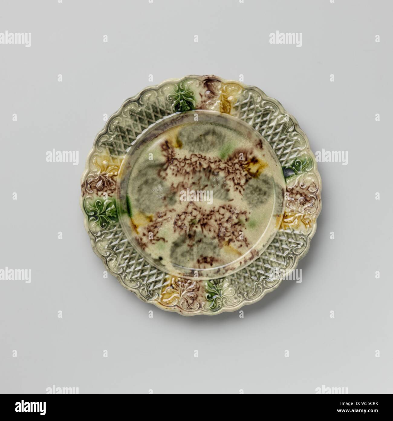 Platte von bunten Hard- abgefeuert, Steingut, Staffordshire, Platte von bunten Hard- feuerte Steingut. Die Grenze ist mit Verzierung, mit zwei symmetrischen floralen Mustern durchsetzt geprägte nebeneinander platziert. Die gekerbte Kante ist auf der Innenseite mit Voluten und Blattmotiven dekoriert. Die Platte ist mit eine gefleckte führen in Mangan Glasur, Grün, Grau und Gelb. Der Rücken ist in Mangan punktiert und hat einen Fuß Flanke, anonym, England, C. 1750 - C. 1780, Steingut, führen Glasur, h 1,6 cm x T 19,3 cm Stockfoto