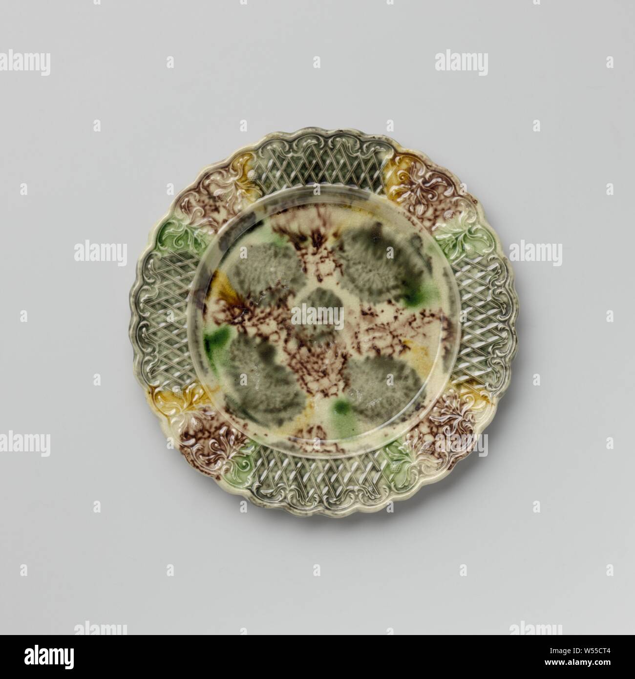 Platte von bunten Hard- abgefeuert, Steingut, Staffordshire, Platte von bunten Hard- feuerte Steingut. Die Grenze ist mit Verzierung, mit zwei symmetrischen floralen Mustern durchsetzt geprägte nebeneinander platziert. Die gekerbte Kante ist auf der Innenseite mit Voluten und Blattmotiven dekoriert. Die Platte ist mit eine gefleckte führen in Mangan Glasur, Grün, Grau und Gelb. Der Rücken ist in Mangan punktiert und hat einen Fuß Flanke, anonym, England, C. 1750 - C. 1780, Steingut, führen Glasur, h 1,6 cm x T 19,3 cm Stockfoto