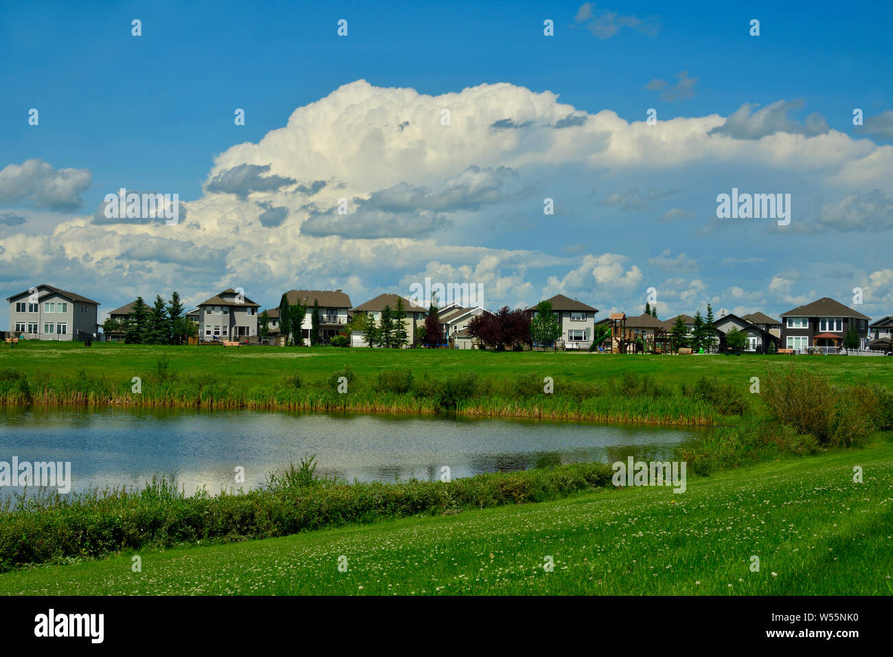 Eine horizontale städtische Landschaft mit einem grünen Raum, die Häuser und die Wolke erfüllte Himmel in der Nähe von Edmonton, Alberta, Kanada. Stockfoto