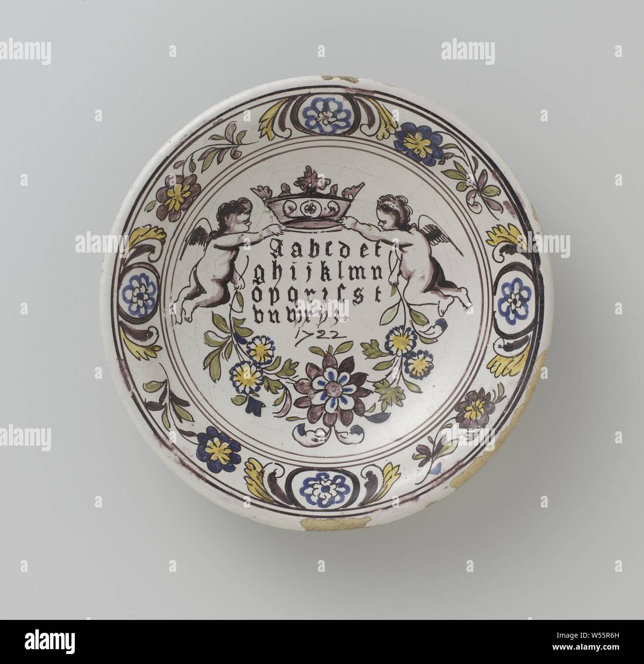Untertasse mit Alphabet gotische Buchstaben und Jahr 1722, runde Untertasse von bunt bemalten Majolika. Zwei Engel sind auf der Untertasse gemalt, mit einer Krone in der einen Hand und hält Blume, blättert in der Anderen, in dem das Alphabet gotische Buchstaben und das Jahr 1722 geschrieben wird., anonym, Makkum, 1722, Keramik, Zinn, Blei Glasur Glasur, d 25,0 cm Stockfoto