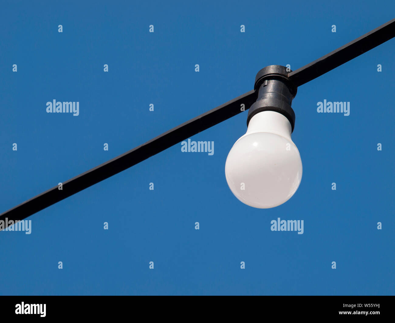 Eine einzelne weiße Einfache Glühbirne auf blauen Himmel Hintergrund hängen von einem schwarzen Netzkabel closeup, Licht ausgeschaltet. Energiesparende Beleuchtung Stockfoto