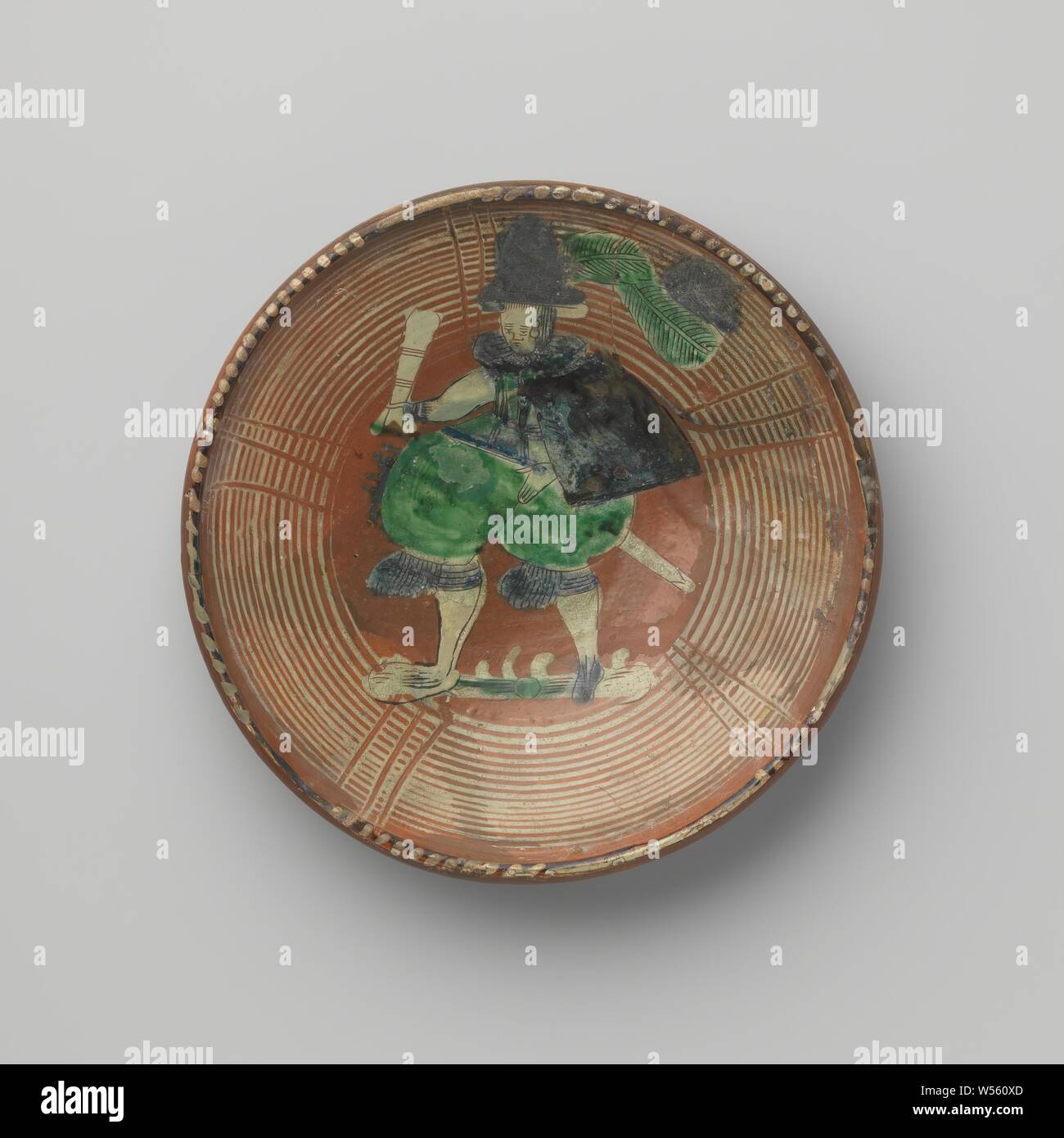 Untertasse, runde Untertasse aus Blei verglaste Steingut. Die volle Länge der Mensch ist auf der Untertasse gemalt. Der Mann trägt einen Hut mit zwei großen Federn, eine Weste, einen rohrmanschette, einer Schulter, Mantel, Hose und Strumpfhalter mit Rüschen. In der rechten Hand hat er ein Glas und auf seiner linken Hüfte ein Schwert. 15 konzentrische Kreise entlang der Kante laufen, mit Linien durch in einigen Orten verstreut., anonym, Wanfried, C. 1600, Steingut, führen Glasur, d 26,7 cm x H 4,9 cm Stockfoto