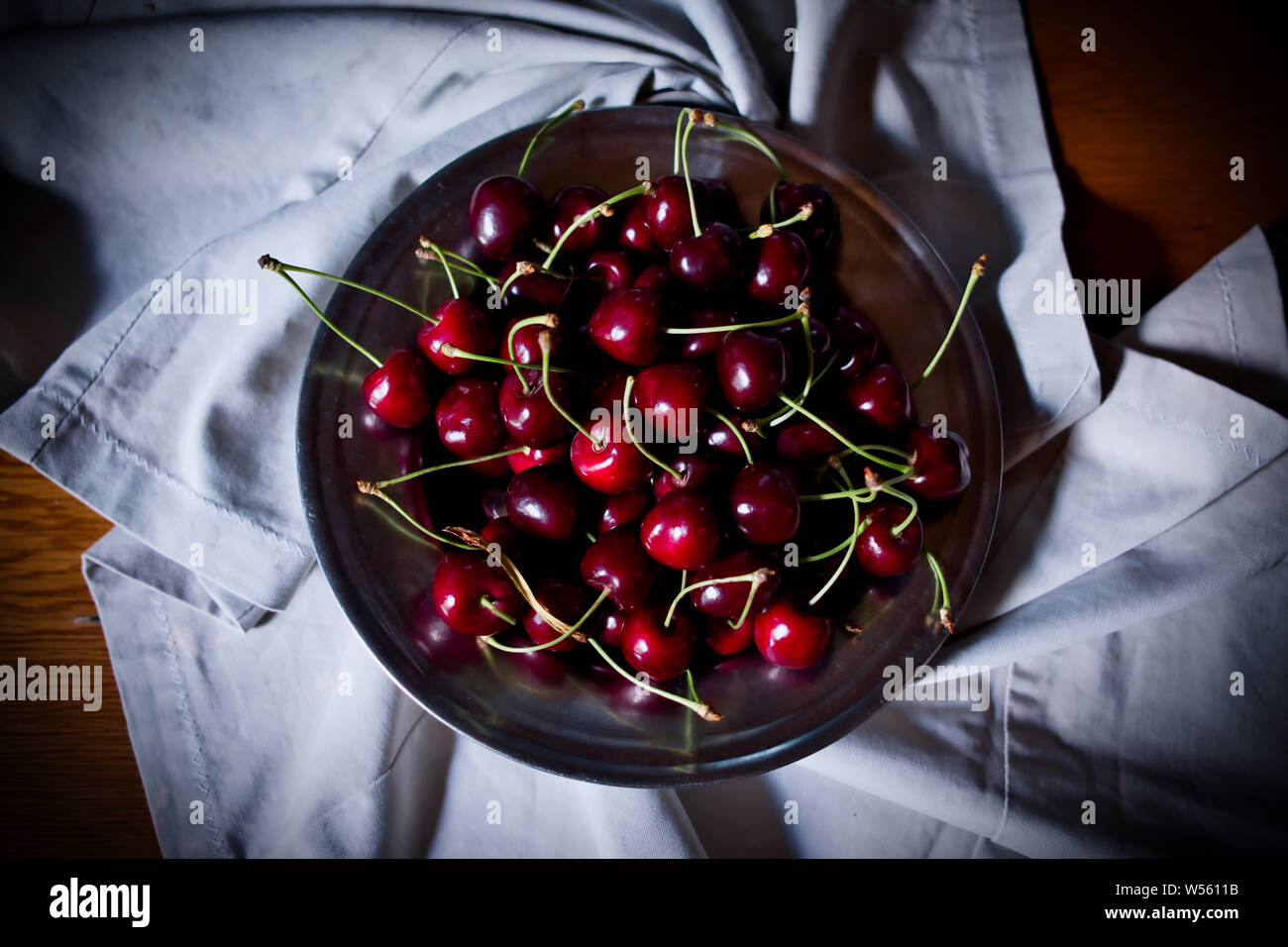 Kirsche, rote reife Kirschen in Platte und auf Stoff, Low Key oder dunkle Fotografie Stockfoto
