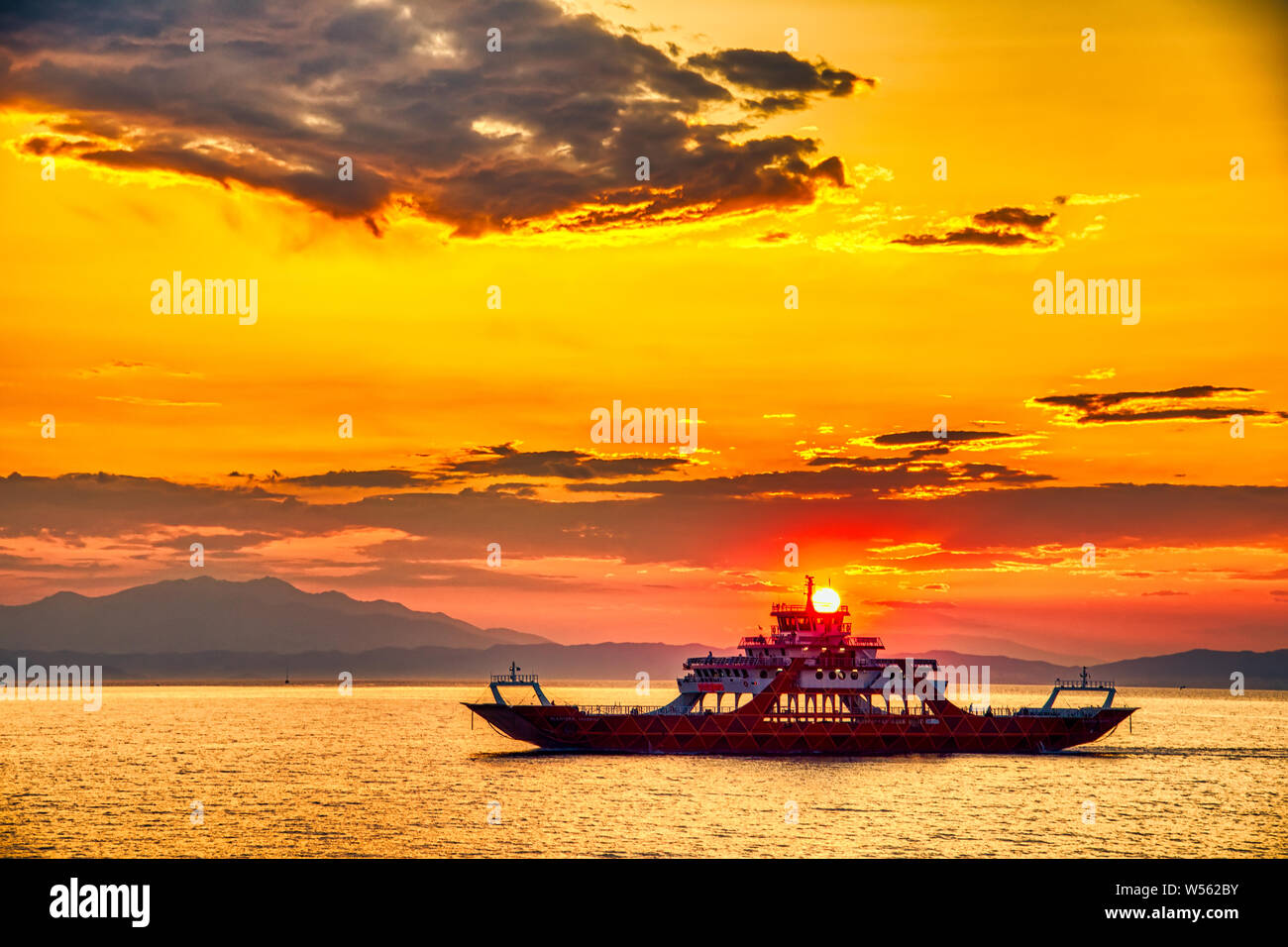 Fähre zum Meer bei Sonnenuntergang im Hintergrund auf die Berge und die Sonne strahlen, Ausführen von Keramoti Stadt auf der Insel Thassos in Griechenland Stockfoto