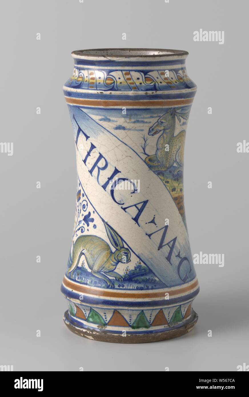 Albarello mit Beschriftung TIRICA MAG, auf eine diagonale Förderband gemalt. Über die Band ein Hirsch, darunter einen Hasen., konkav zylindrische Vase mit engem Hals und Fuß, aus bunten Majolika-fliesen. Eine diagonale Förderband ist auf die Vase mit der Aufschrift gemalt: TIRICA MAG. Ein Reh ist über die Band lackiert und ein Hase ist unterhalb der Band. Die Vase ist weiter mit floralen blättert gemalt., Huftiere: Reh, Nagetiere: Hase, anonyme, Antwerpen, C. 1525 - C. 1560, Steingut, Zinn, Blei Glasur Glasur, h 26,0 cm x T 12,5 cm Stockfoto