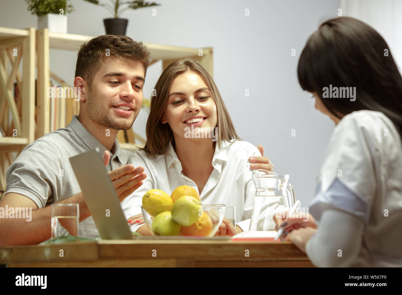 Lächelnd Ernährungssachversta5ndiger zeigt eine gesunde Diät Plan und Früchte zu Patienten. Junges Paar besucht ein Arzt für eine Ernährung Empfehlungen. Gesunde Lebensweise und Ernährung, Medizin und Behandlung. Stockfoto