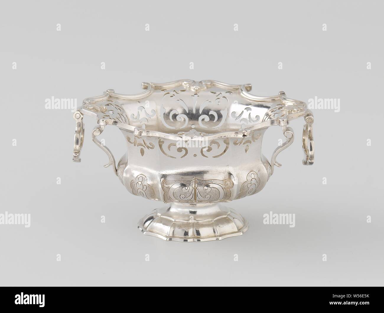 Candy, die längliche Zweifachdose hat zwei Ohren mit schwenkbaren Griffen. Die Basis besteht aus einem Muschelförmigen, gewölbt, verjüngenden Abschnitt, ruht auf einem niedrigen Sockel und eine glatte, verengte Abschnitt bildet die Verbindung zum Behälter, die wieder überbacken wird. Die Mauer des Schiffes ist konvex und konkav. Der konvexe Teil ist mit einer Gravur Dekoration der Blume Glocken und Voluten auf Scalloped, aufgeraut. Die hohle Teil hat gesägt -, Dekoration, symmetrische Muster, aus voluten, Ventilator Formen und anderen Elementen gebaut. Sowohl die eingraviert und die ABGESÄGTE-out Dekorationen sind Stockfoto