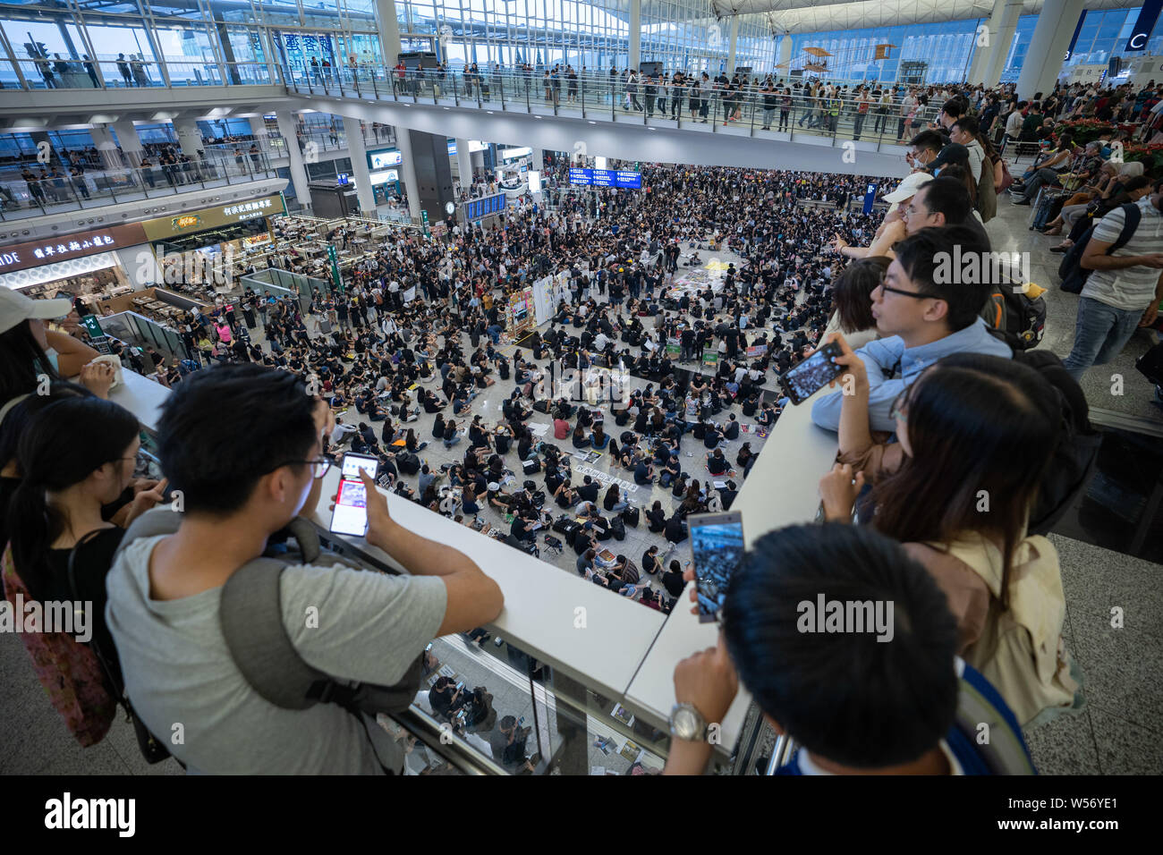 Touristen vom Festland China verwenden ihr Handy Bild zu nehmen, wie tausende Demonstranten einen Protest an der Hong Kong International Airport Ankunft Halle sitzen. Tausende von Demonstranten gegen die Regierung inszenierten einen Protest an der Hong Kong International Airport terminal Sitzen, das erste von drei geraden Tagen Demonstrationen nach Auseinandersetzungen in der vergangenen Woche ausgelöst wird befürchtet, dass eine breitere Auseinandersetzung in der Stadt ausbrechen könnte. Stockfoto