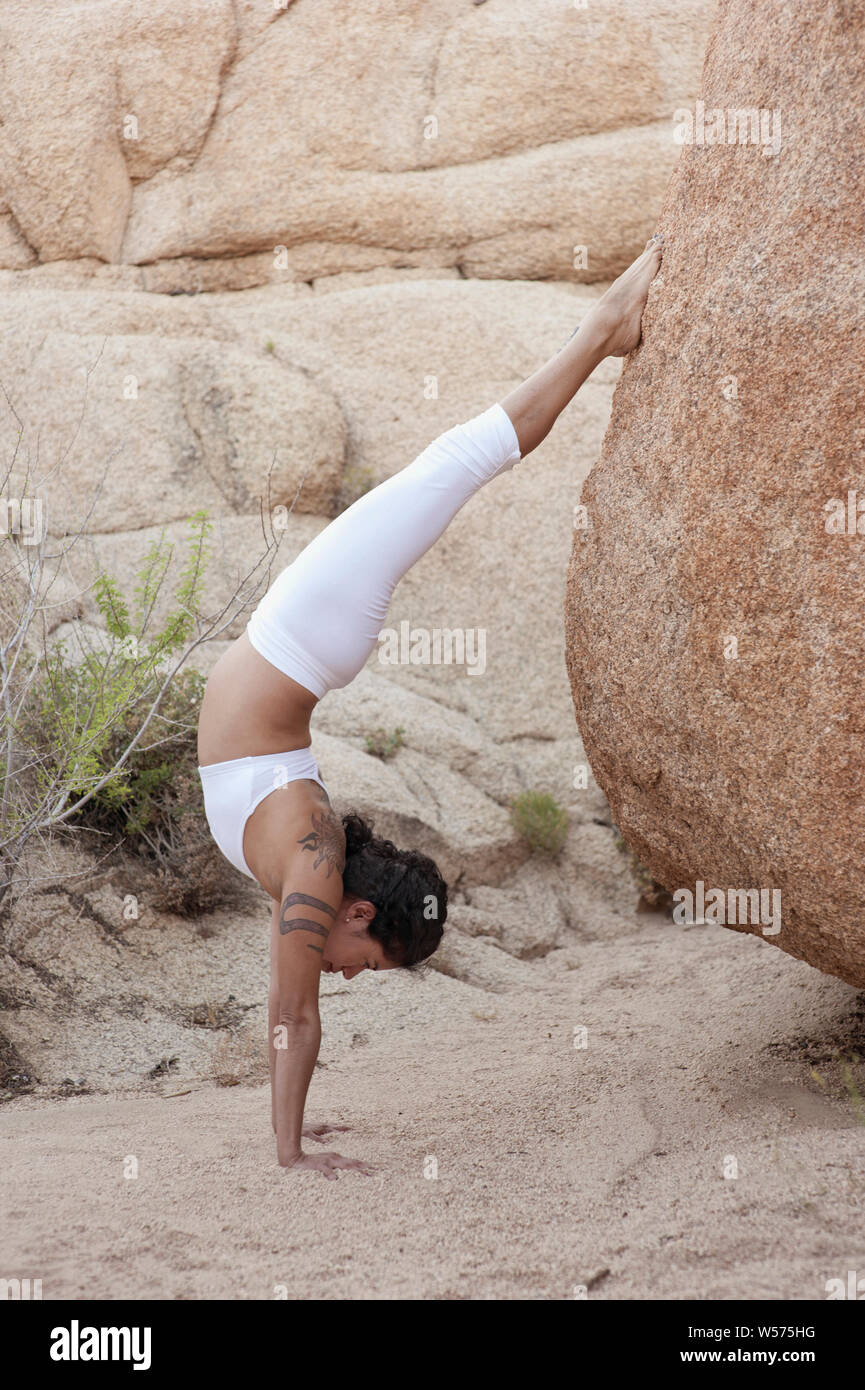 Hispanic yogini in einem unterstützten Handstand in der Natur. Stockfoto