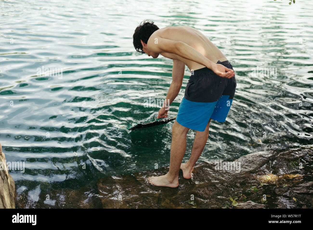 Junger Mann in Beach Shorts Waschmaschine Grill in einem Fluss Stockfoto
