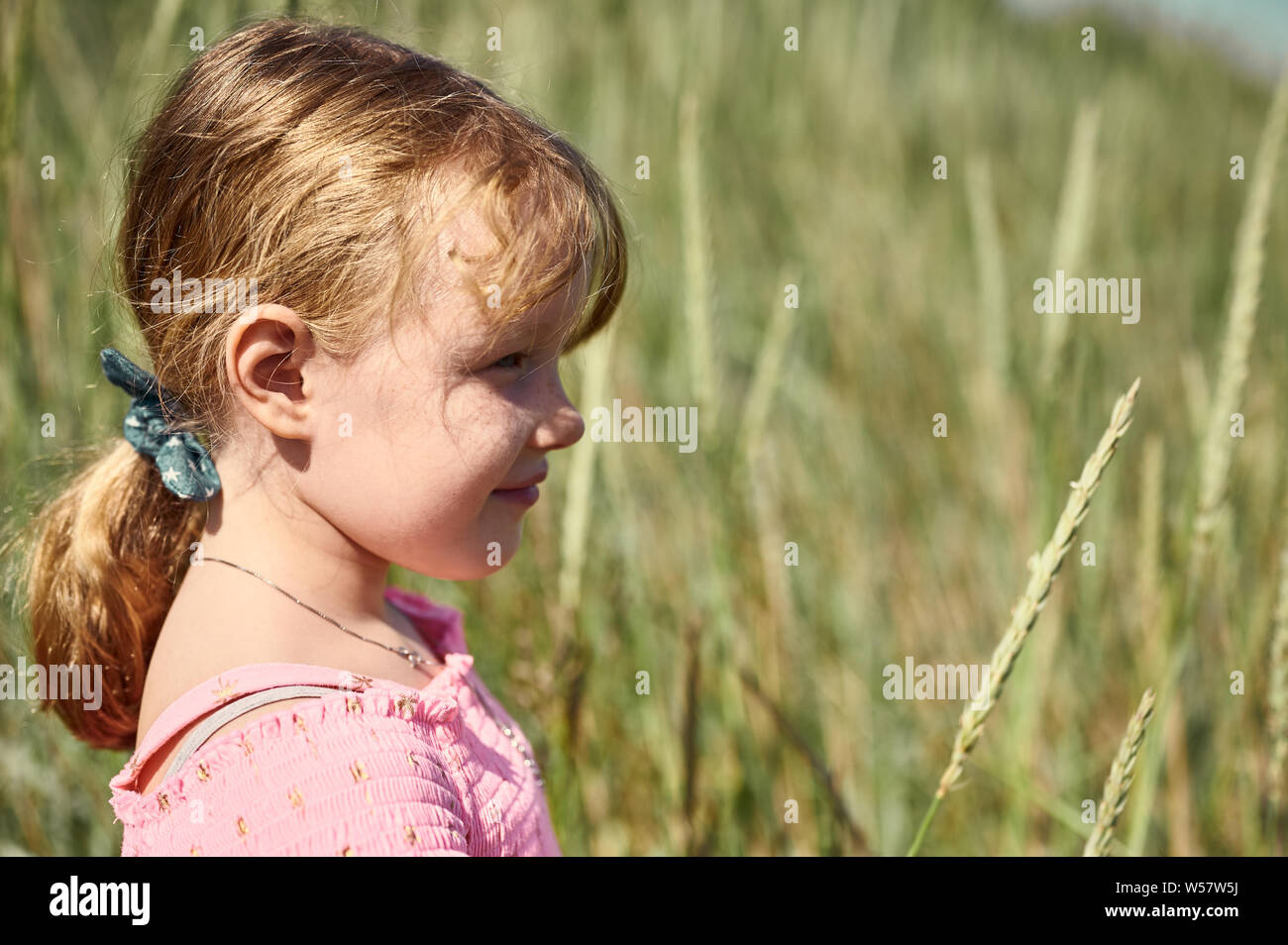 Seitenansicht des kleinen adorable blonde Mädchen mit schüchternen Lächeln im Feld auf Grotta Insel auf unscharfen Hintergrund Stockfoto