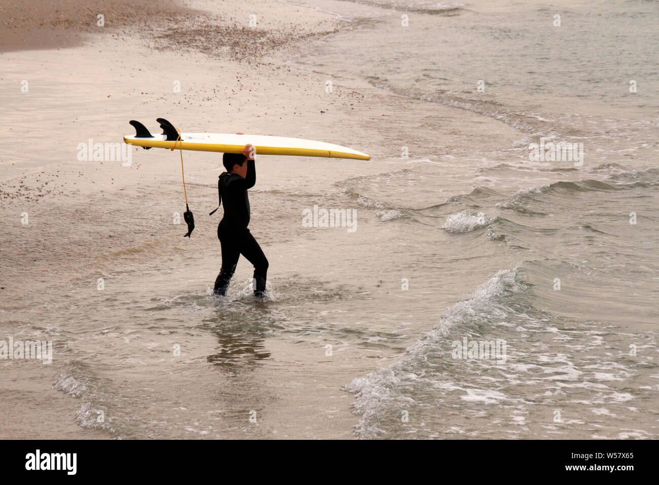 Ein kleiner Junge in einen Taucheranzug trägt sein Surfbrett in das Mittelmeer entlang der Strand in Tel Aviv. Stockfoto