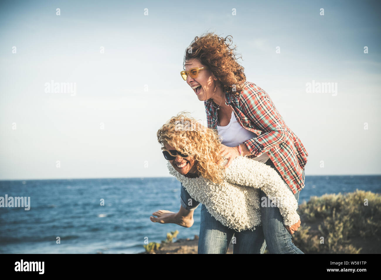 Porträt von zwei hübsche Frau, die freie Zeit genießen. Lächelnd mittleren Alter Mädchen, die ihr Lachen Freund piggyback während den Tag gemeinsam Spaß an der Bea Stockfoto