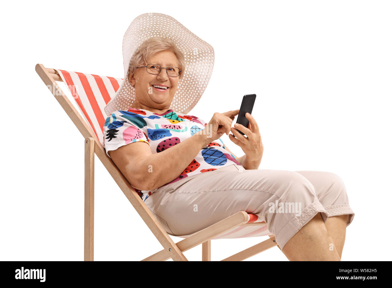 Ältere Frau auf einen Urlaub mit einem Telefon im Liegestuhl sitzen, und wenn man die Kamera auf weißem Hintergrund Stockfoto