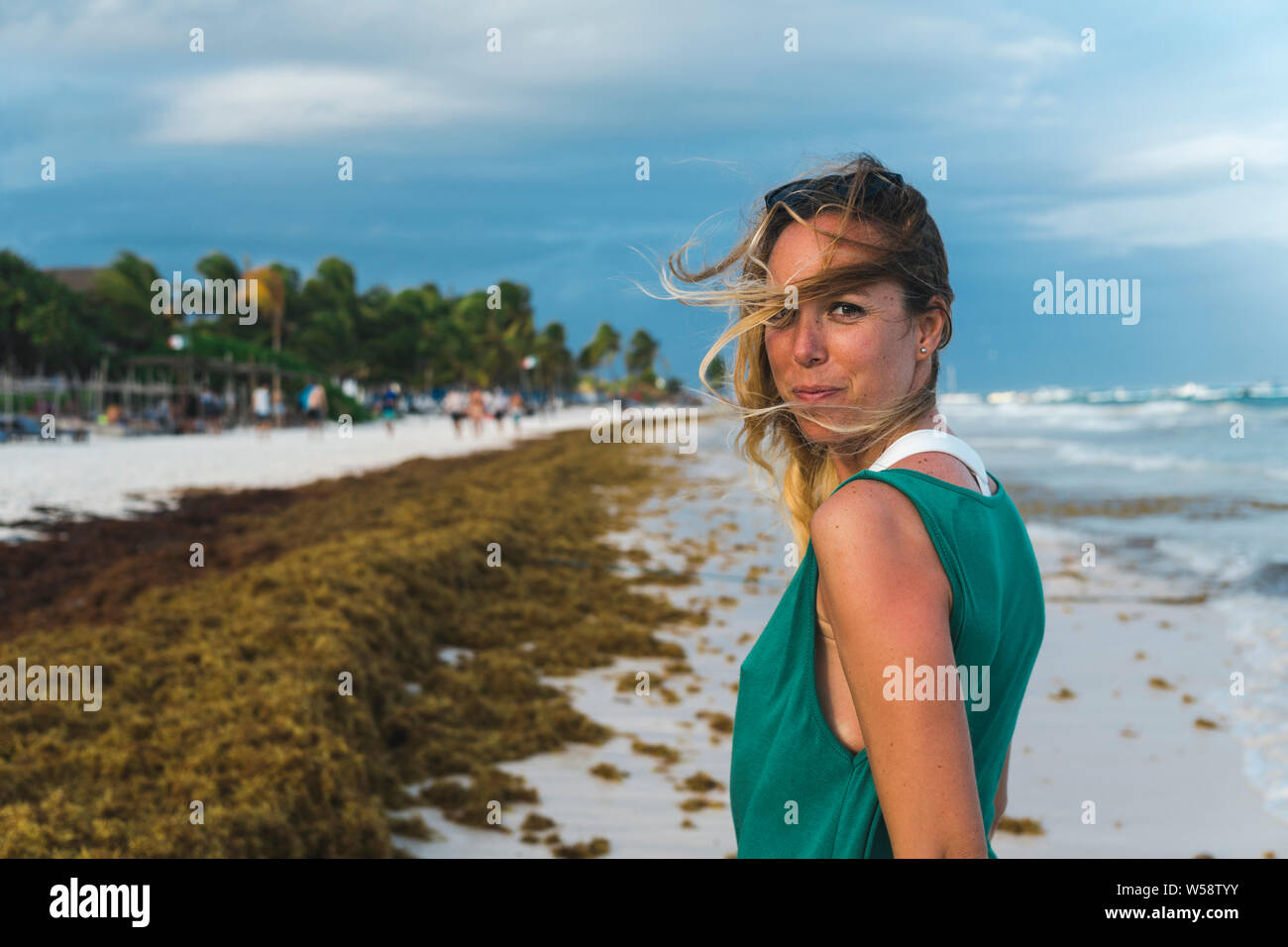 Schöne erwachsene Frau fröhlich lächelnd auf windigen Strand bei Sonnenuntergang Stockfoto