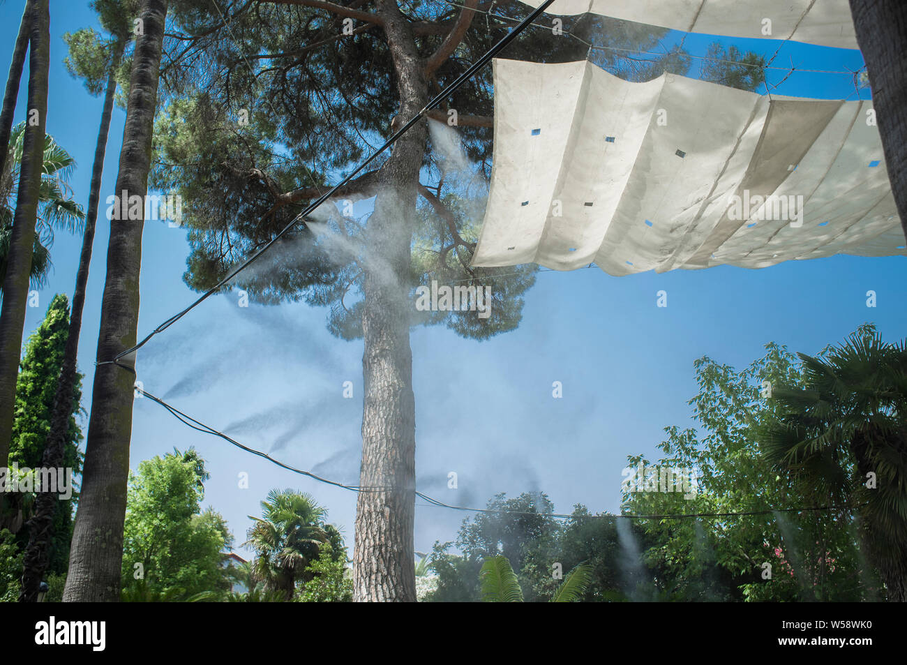 Markise und Sprinkler spritzt verdampft Wasser bei öffentlichen Park. Geräte für die Kühlung der heißen Sommer Temperatur in Spanien im Freien Stockfoto