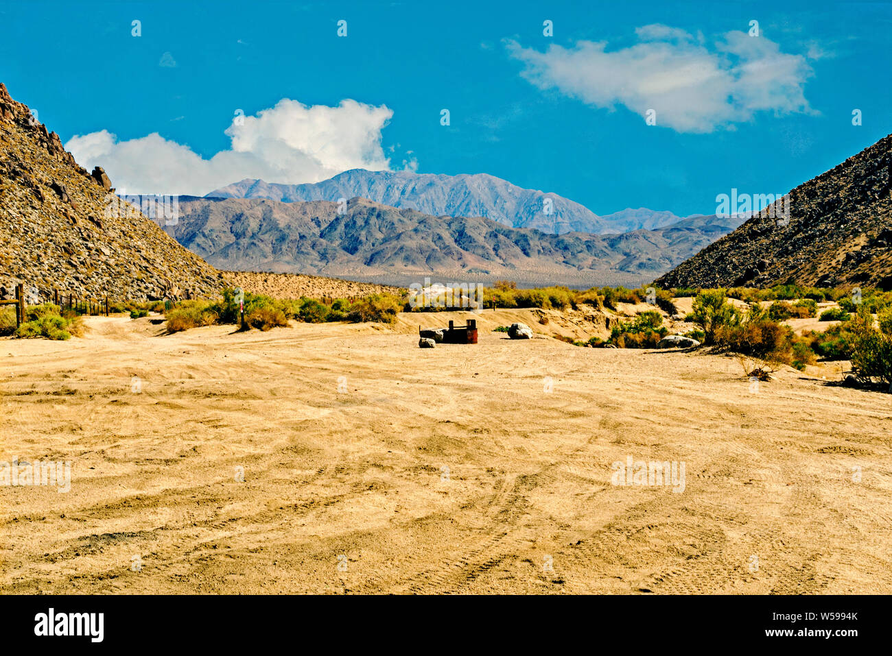 Gelb Braun Sandy Desert Talboden mit spärlicher Vegetation wachsen in zwischen zwei kargen Berge mit blauen unfruchtbaren Bergen reicht darüber hinaus, blauer Himmel. Stockfoto