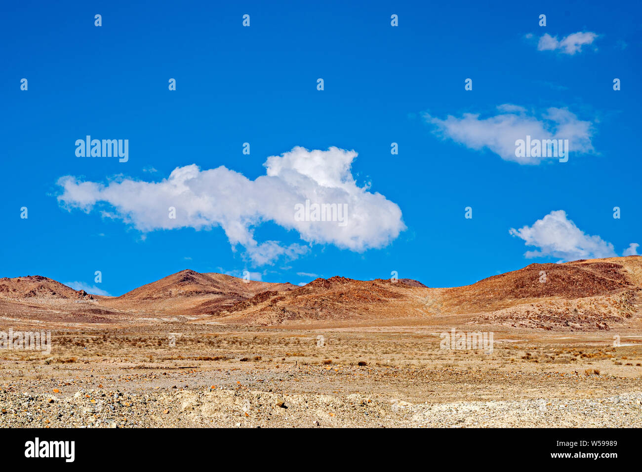 Braun öde Wüste Tal mit Hügeln unter strahlend blauen Himmel mit weißen Wolken. Stockfoto