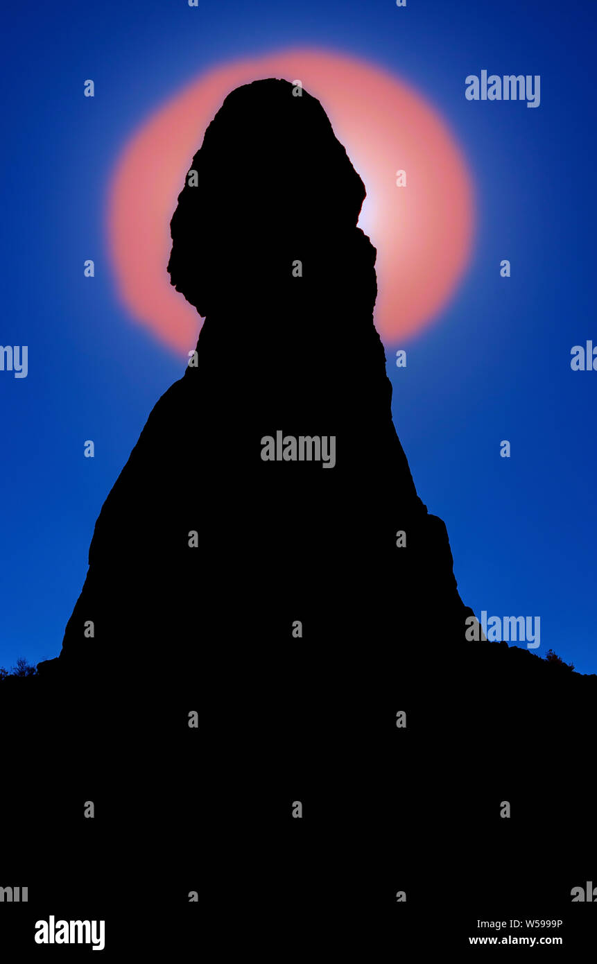 Groß rock Pinnacle mit abgerundetem Kopf, rot orange Kreis des Lichtes direkt hinter der Felsformation. Pinnacle ist mit einer Hintergrundbeleuchtung ausgestattet, mit blauem Himmel. Stockfoto